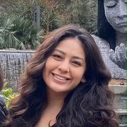 Portrait of Sarah Ceja smiling outdoors in front of greenery and a stone sculpture