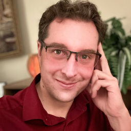 Man wearing glasses and a red shirt, smiling at the camera