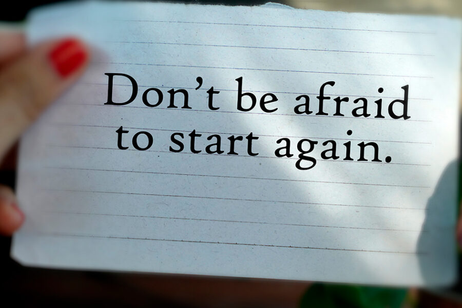 Motivational note reading, “Don’t be afraid to start again,” held by a person’s hand on lined paper.