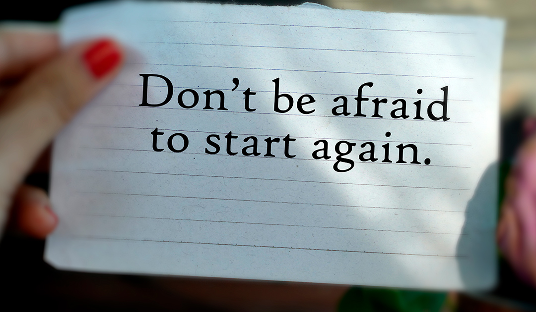 Motivational note reading, “Don’t be afraid to start again,” held by a person’s hand on lined paper.