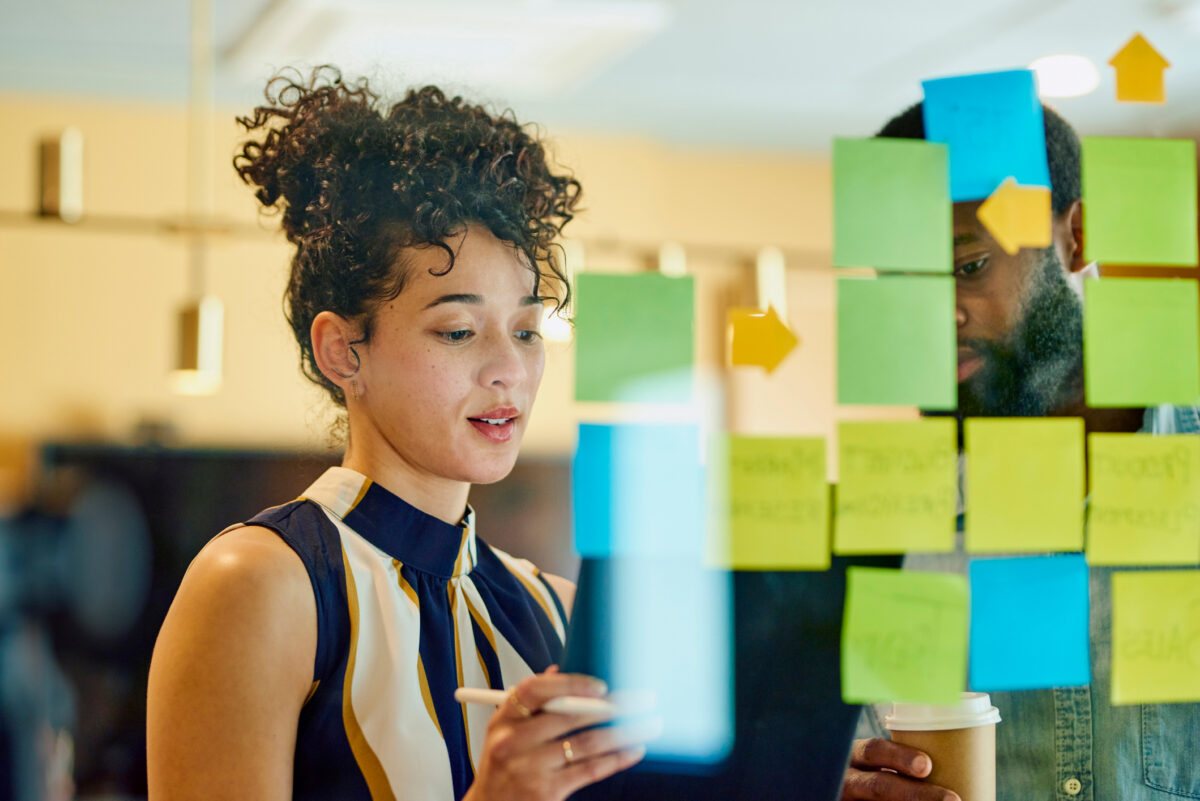 Two coworkers discussing ideas through sticky notes on a glass wall