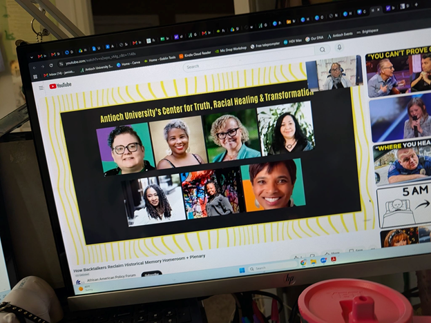 Computer monitor displaying an Antioch University Center for Truth, Racial Healing & Transformation presentation featuring headshots of seven participants.