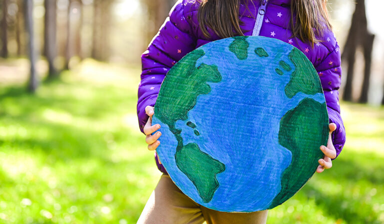 Child holding a hand-drawn globe in a sunlit park