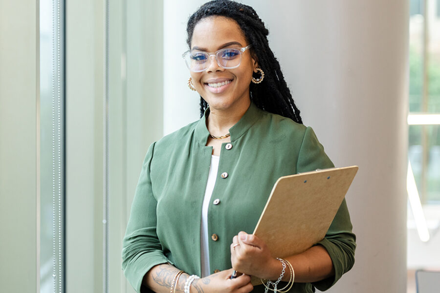 Smiling woman wearing glasses holds a clipboard in a bright office