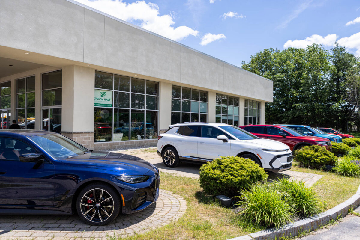 Exterior of a commercial building with large windows, a Green Wave sign, and several parked cars