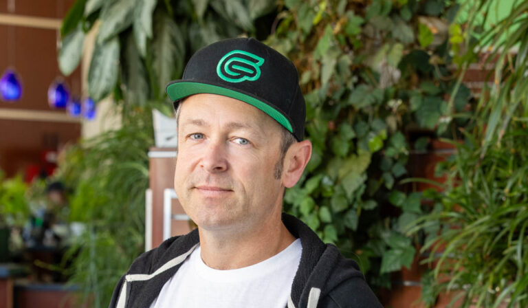 Man wearing a black-and-green cap and hoodie standing among plants