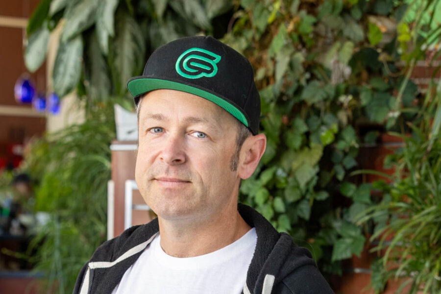 Man wearing a black-and-green cap and hoodie standing among plants