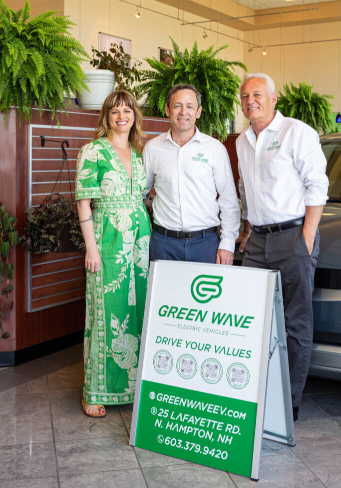 Three Green Wave Electric Vehicles representatives stand behind the company’s sign in a showroom