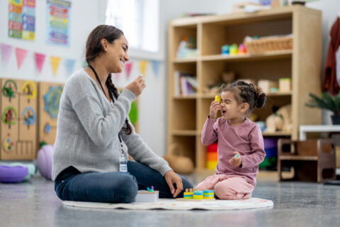 Teacher and young girl sit on a classroom floor, playing with colorful blocks